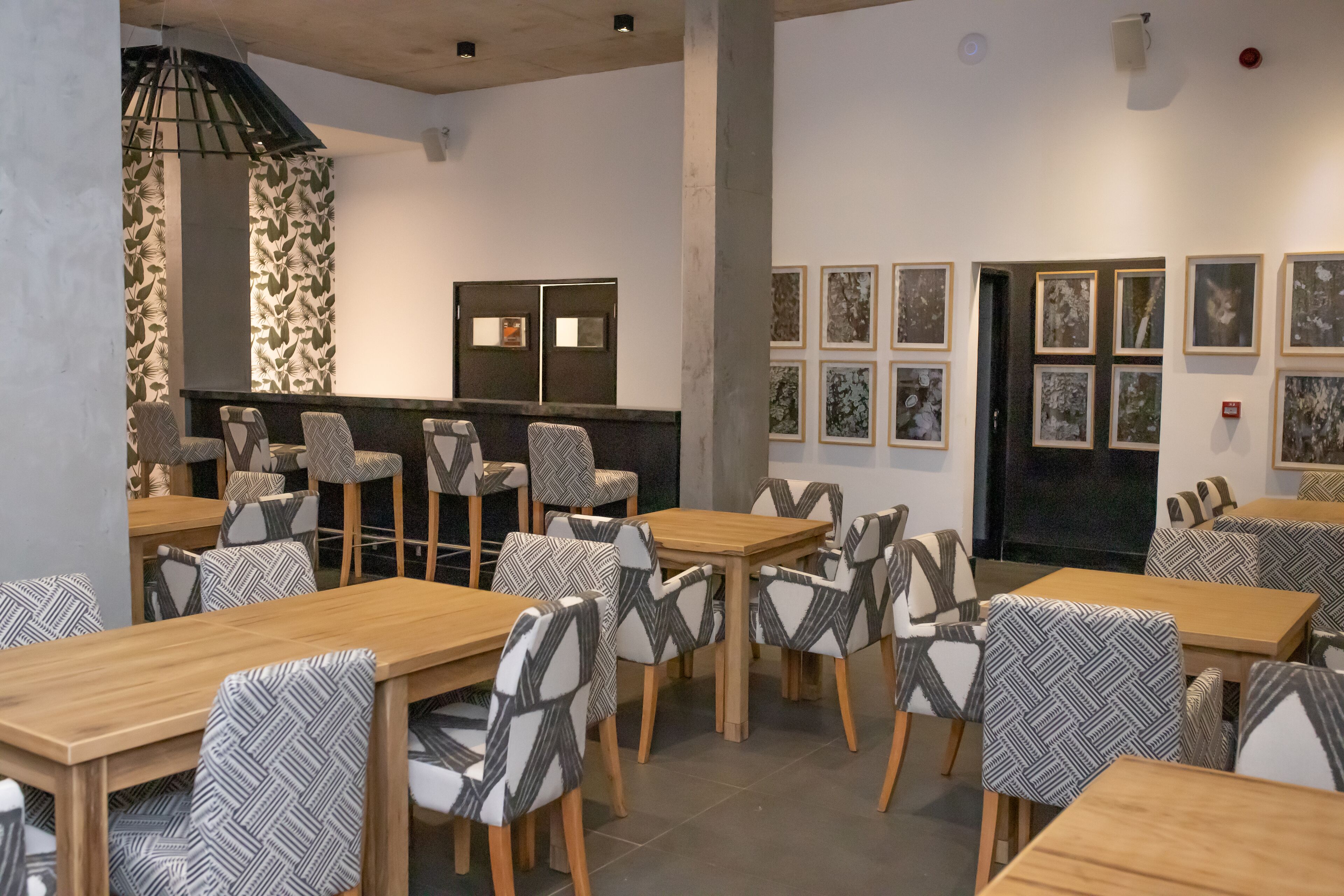 A modern dining area with wooden tables and patterned chairs, a stone wall, and framed artwork on the walls.