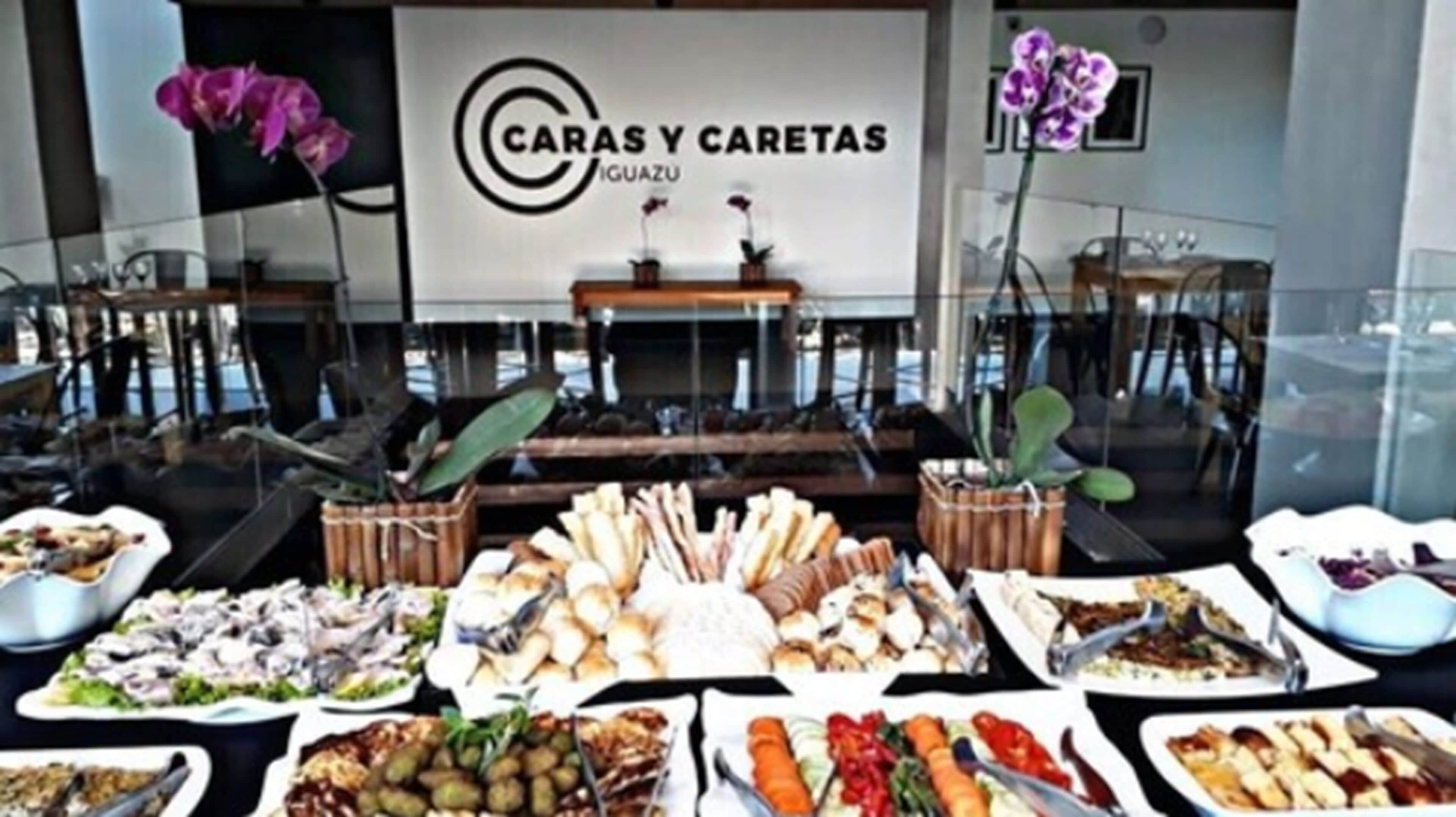 Montaje de bufé con diversas opciones de comida y un letrero que dice "CARAS Y CARETAS IGUIAZU".