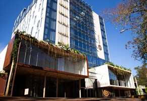Un hotel moderno con fachada de vidrio, zona de estar al aire libre y plantas en los balcones.