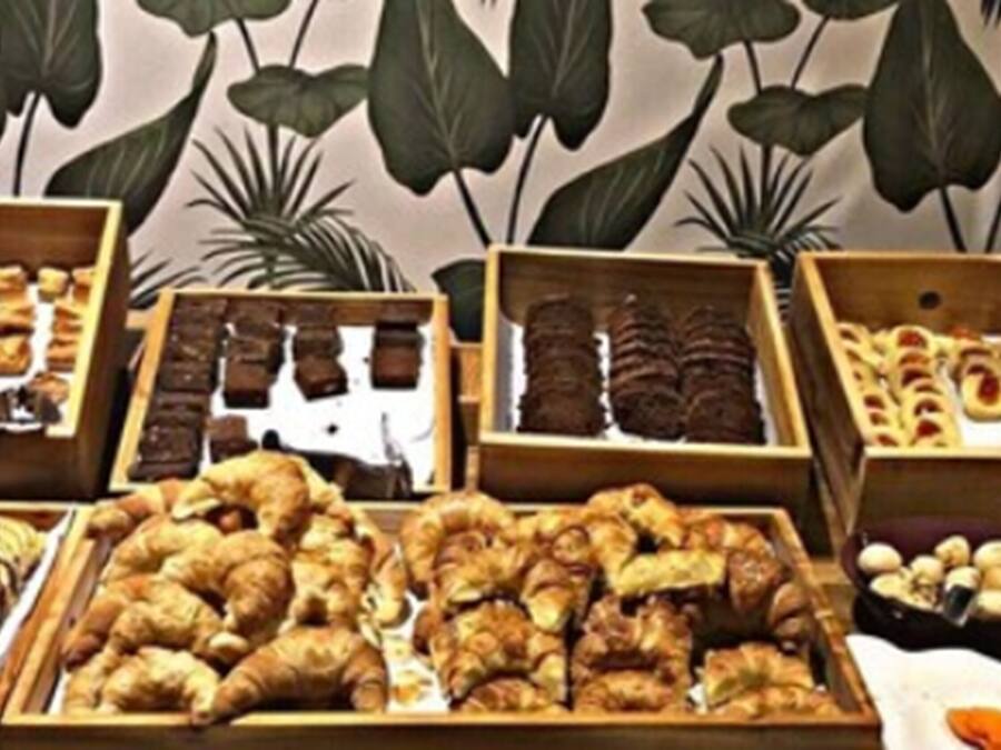 A variety of baked goods displayed in wooden boxes, including pastries and bread, arranged on a table with a backdrop of large green leaves.