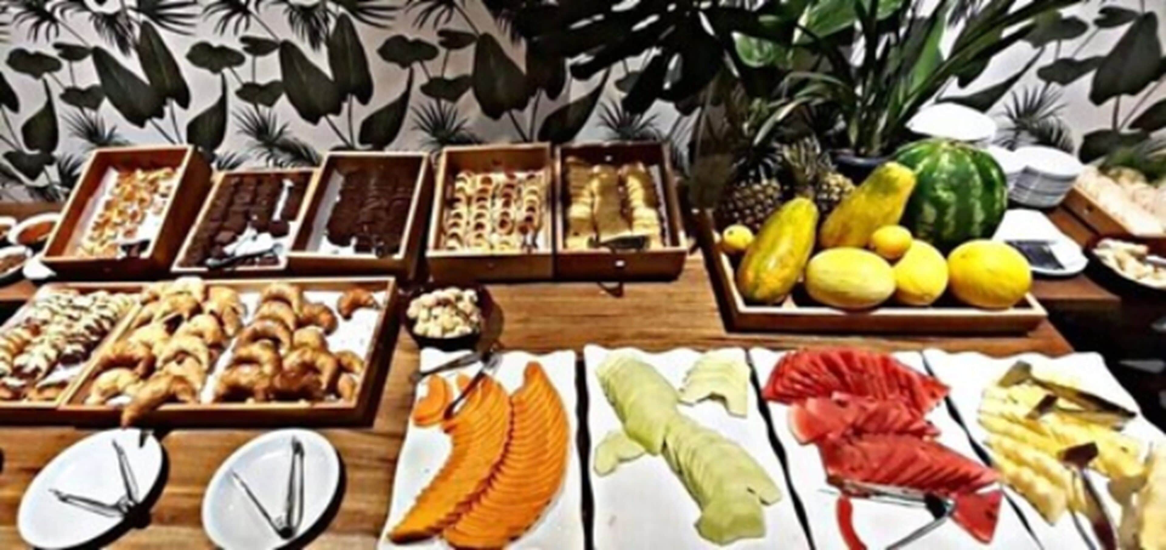 Un bufé con diversos alimentos, entre ellos frutas, bollería y postres.