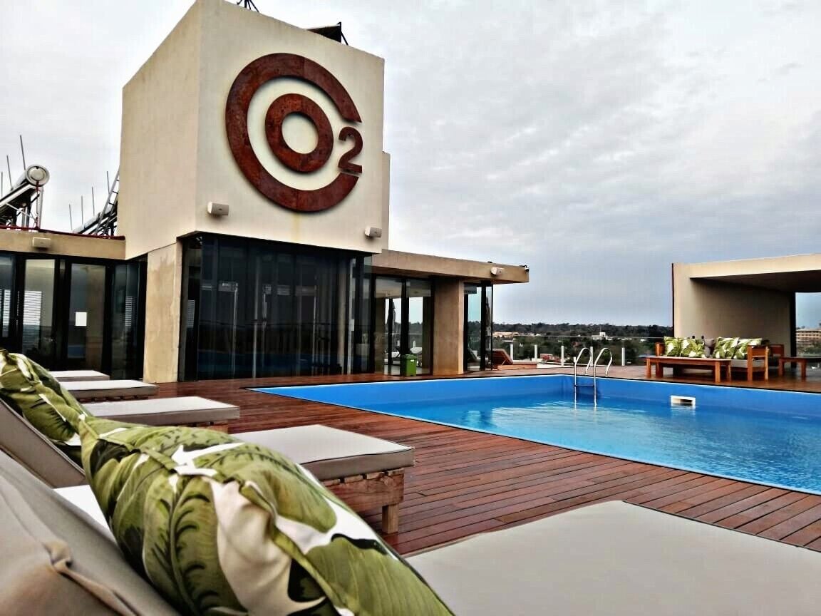 Ein modernes Hotel mit großem Pool, einer Lounge mit Liegestühlen und einem markanten Gebäude mit kreisigem Logo.