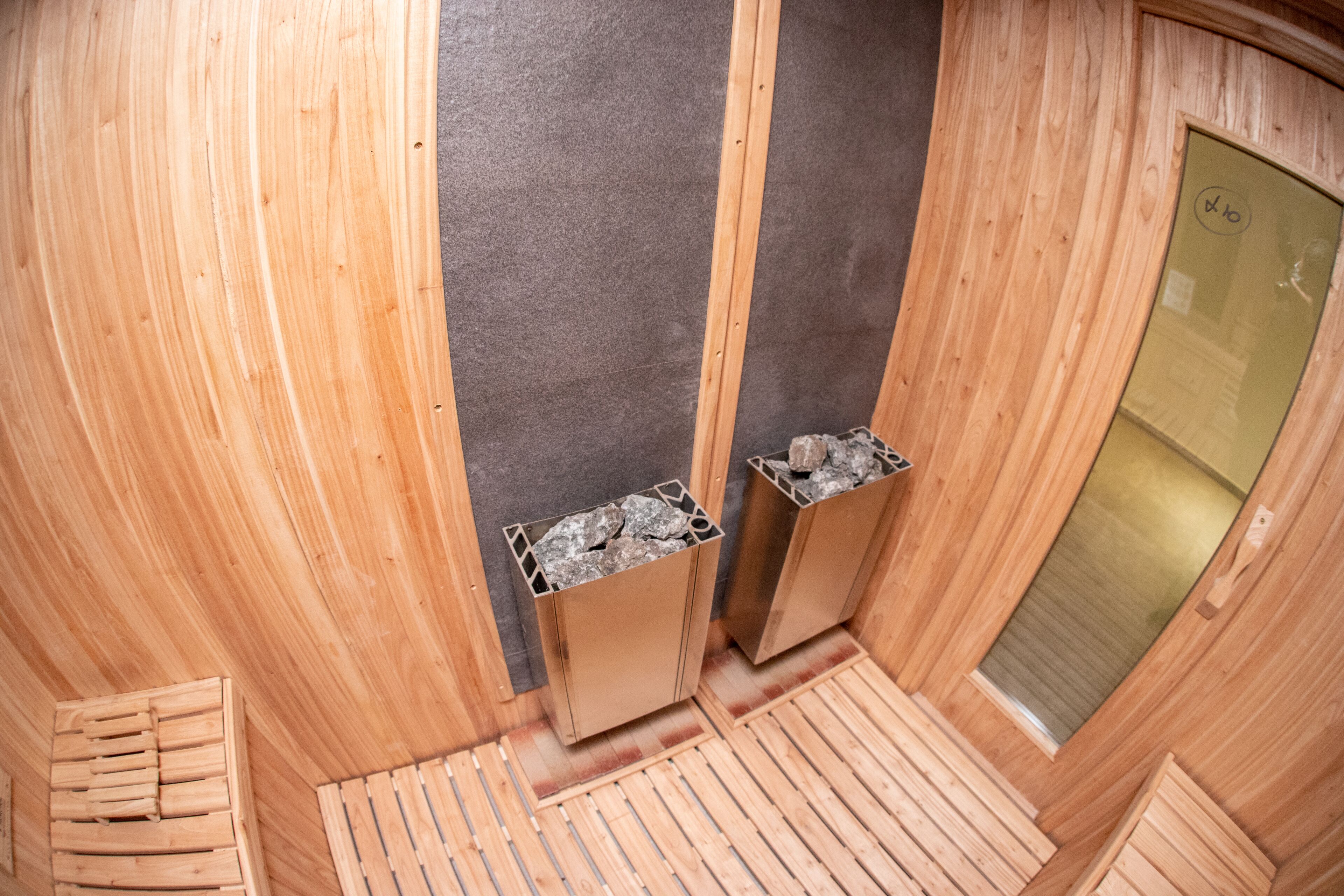 Una sauna con paredes y bancos de madera, una puerta de vidrio y suelo de baldosas.