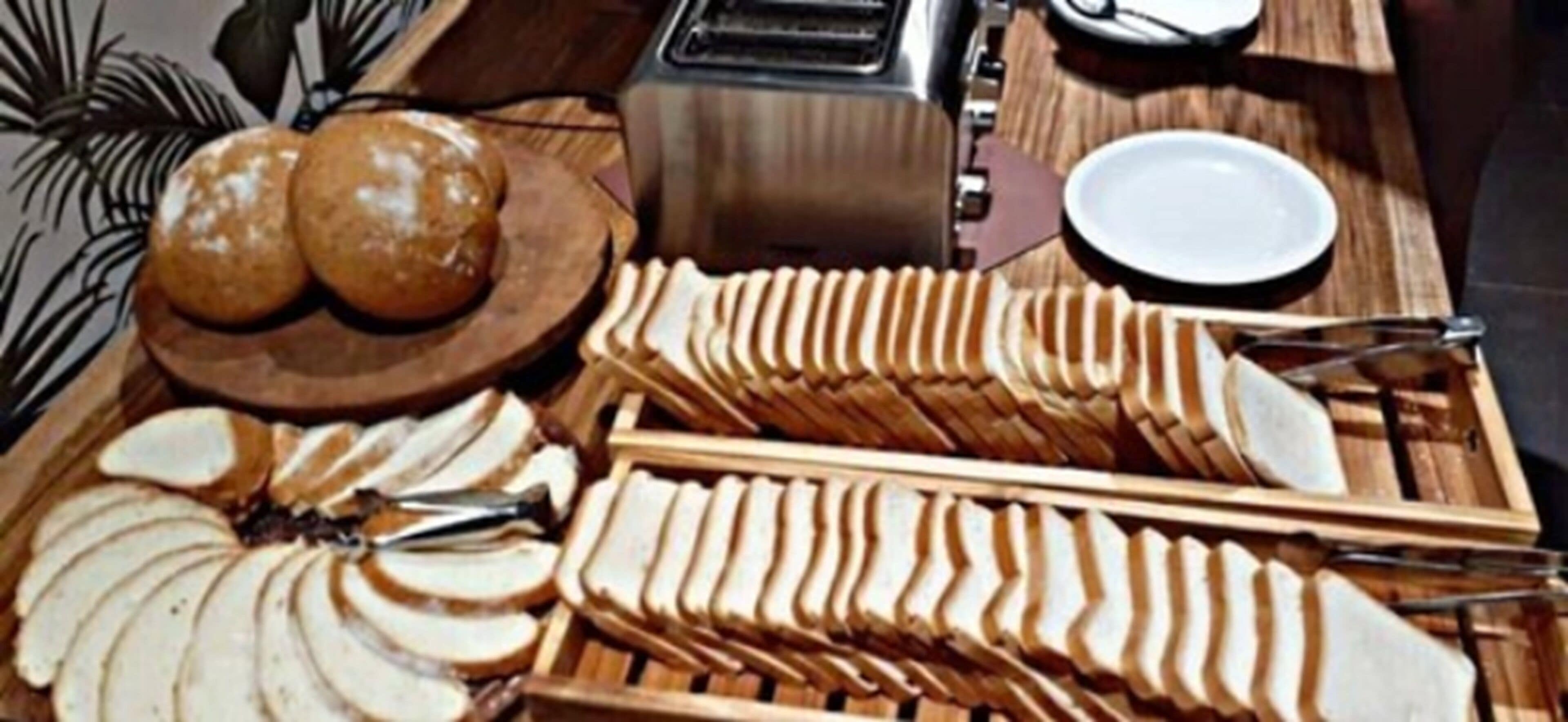 A buffet table with sliced bread, rolls, and a toaster.