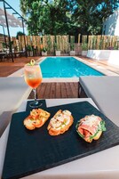 Escena junto a la piscina con una mesa que tiene una bebida y sándwiches.