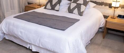 A neatly made bed with a gray throw, two bedside lamps, and a patterned wall.