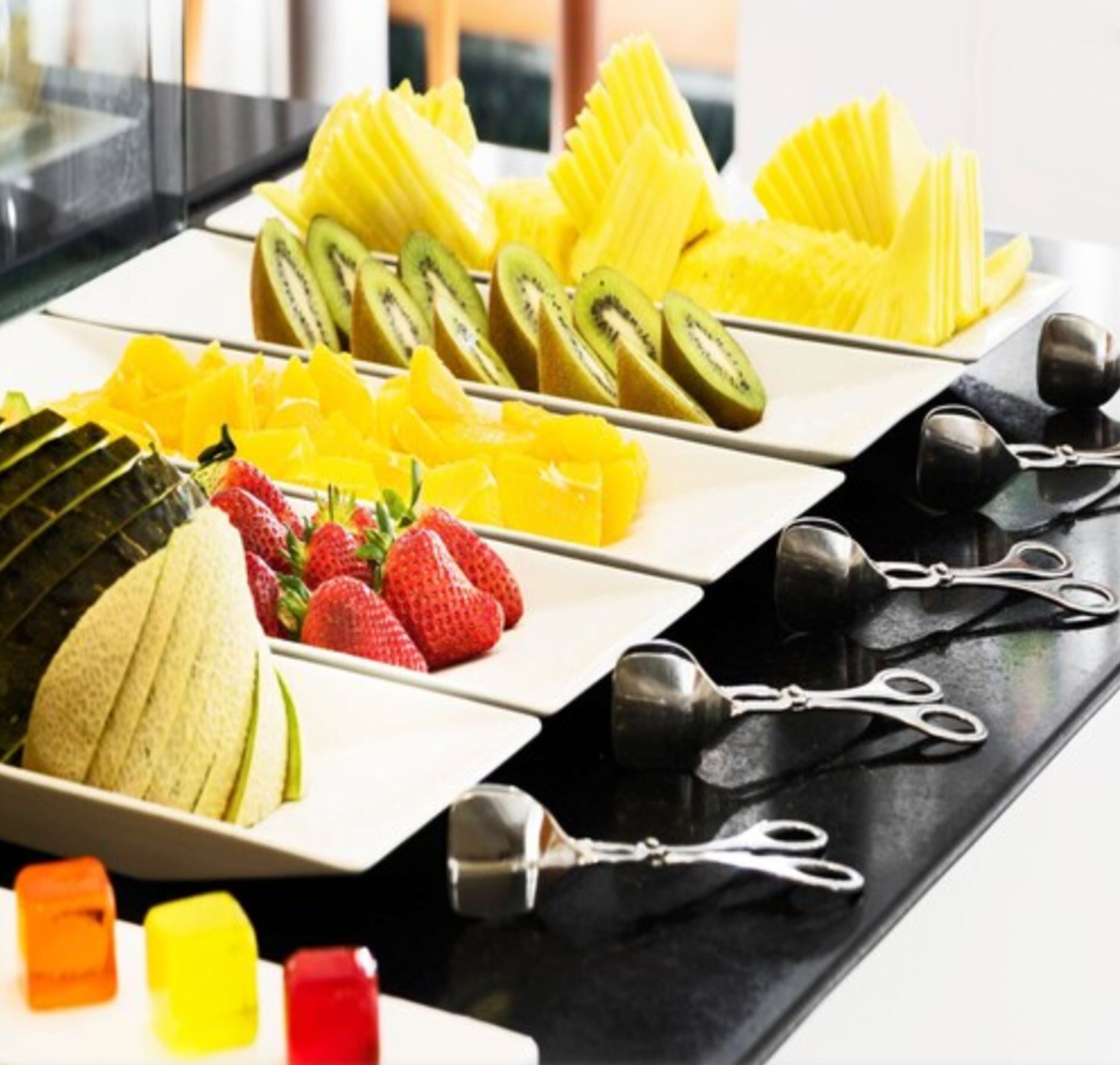 Una exhibición de frutas con kiwi en rodajas, mango, fresas y una piña.
