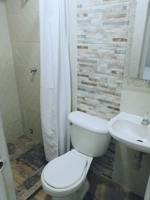 A bathroom with a toilet, a sink, and a shower area. - Hotel Londres Real (Valledupar)