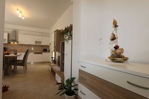 Eine moderne Küche mit weißen Schränken, einem Essbereich mit Tisch und Stühlen sowie einer dekorativen Pflanzengruppe auf der Arbeitsplatte.