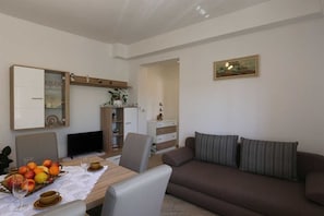 Ein Essbereich mit einem Tisch für zwei Personen, einem braunen Sofa und einem Fernseher.