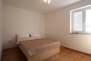 A bedroom with a bed, a window, and a wooden floor. - Apartment Djakovic Boba nr 1 (Silo - island Krk)