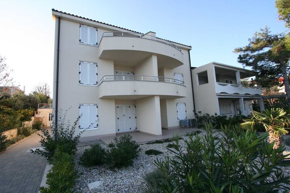 Um edifício com vários andares, varandas, entrada por automóvel e um jardim ajardinado.