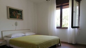 A bedroom with a bed, a nightstand, a painting on the wall, and a window with curtains. - Apartment Grskovic G. Setaliste A4 (Silo - island Krk)