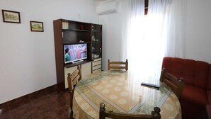 A living room with a glass-top dining table, wooden chairs, a red sofa, a television, and a bookshelf. - Apartment Grskovic G. Setaliste A4 (Silo - island Krk)