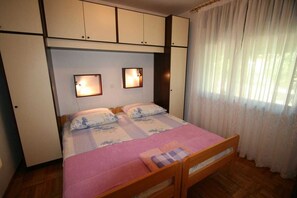 Un dormitorio con una cama, dos lámparas de noche, una ventana con cortinas y un armario.