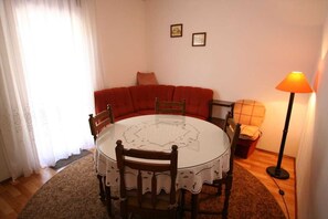 A dining area with a round table, chairs, a red sofa, a floor lamp, and two framed pictures on the wall. - Apartment Grskovic G. Setaliste A4 (Silo - island Krk)