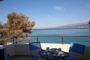 A balcony with a table and chairs, overlooking a body of water and a distant coastline. - Apartment Djakovic Deni 1 (Silo - island Krk)