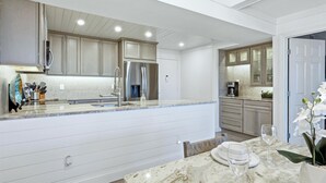 A modern kitchen with white cabinetry, a marble countertop, and stainless steel appliances. - Anchorage Resort 3rd Floor Two Bedroom Condo with Beach Access (Siesta Key)
