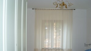 A room with a large window covered by sheer curtains and a decorative lace trim at the bottom. A blue sofa is positioned to the right of the window. - Villa Sandra (Giulianova)