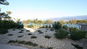 Ein angelegter Garten mit Kieswegen, verschiedenen Sträuchern und Blick auf ein Gewässer sowie ferne Berge.