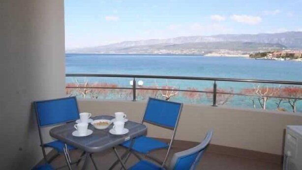 Ein Balkon mit Tisch und Stühlen, der Blick auf die Küste freigibt.