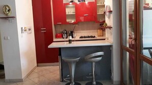A compact kitchen with red cabinets, a small island with stools, and a coffee machine. - 3 bed apartment, 1 bathroom, Large Private Patio & Garden, Mountain views, (Pizzo)
