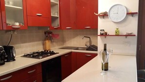 A kitchen with red cabinets, a white countertop, a gas stove, a sink, and a wine glass on the counter. - 3 bed apartment, 1 bathroom, Large Private Patio & Garden, Mountain views, (Pizzo)