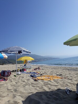 Una spiaggia con ombrelloni, asciugamani e sedie a sdraio.