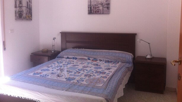 Un dormitorio con cama, mesita de noche, lámpara de pared y una puerta.