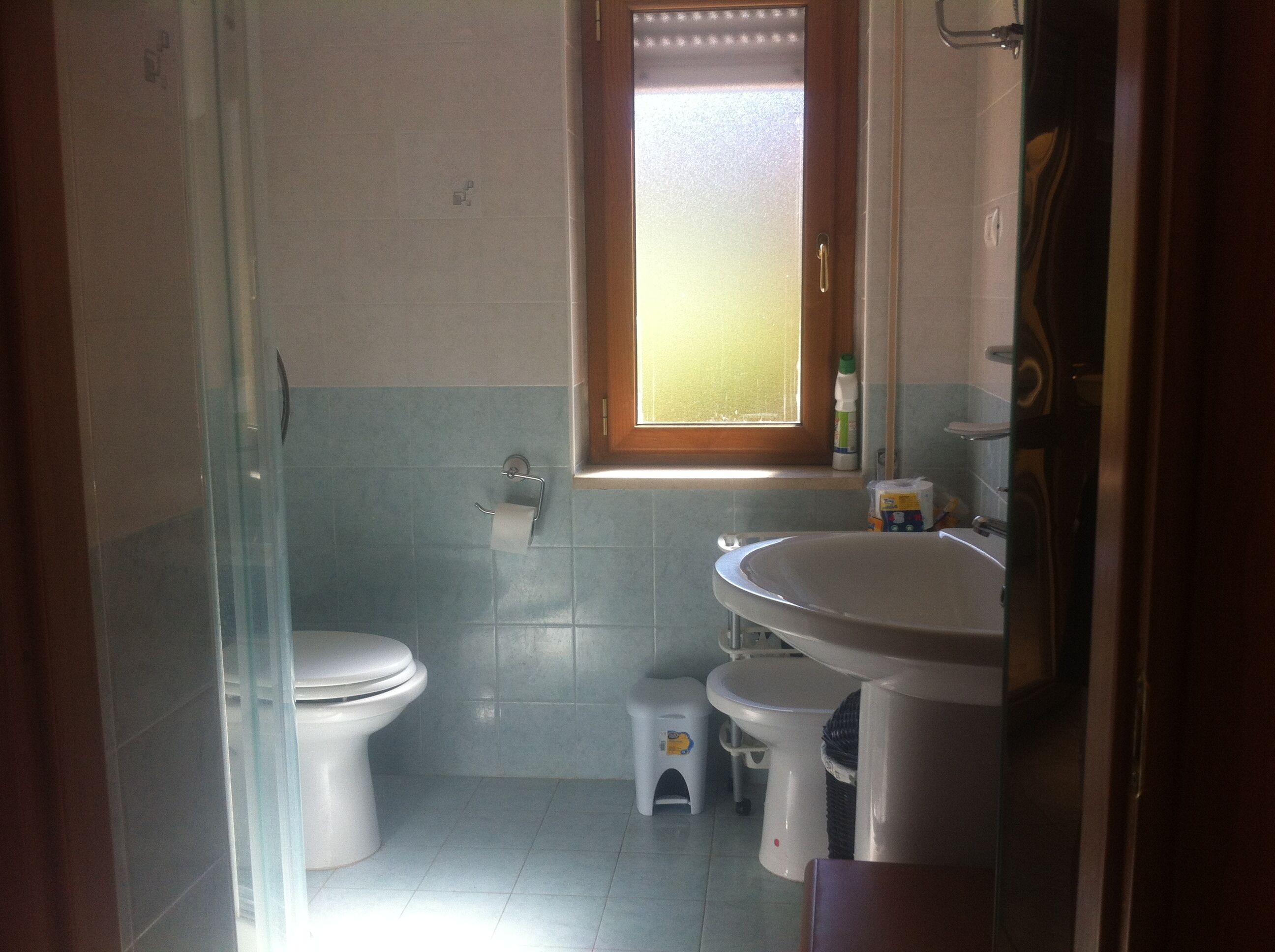 Ein Badezimmer mit Toilette, Waschbecken, einer kleinen Stehgehilfe und einem Fenster.