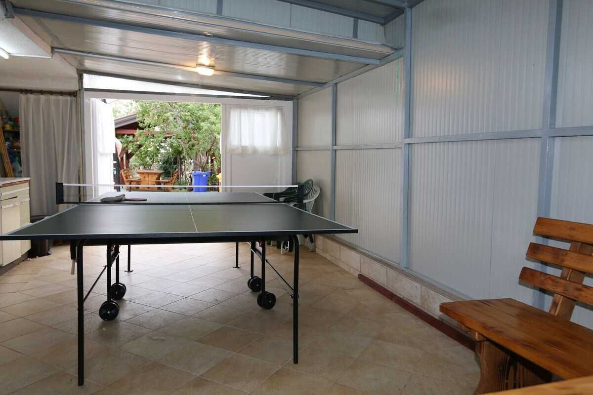 A ping pong table in a room with a view of a garden through a window.
