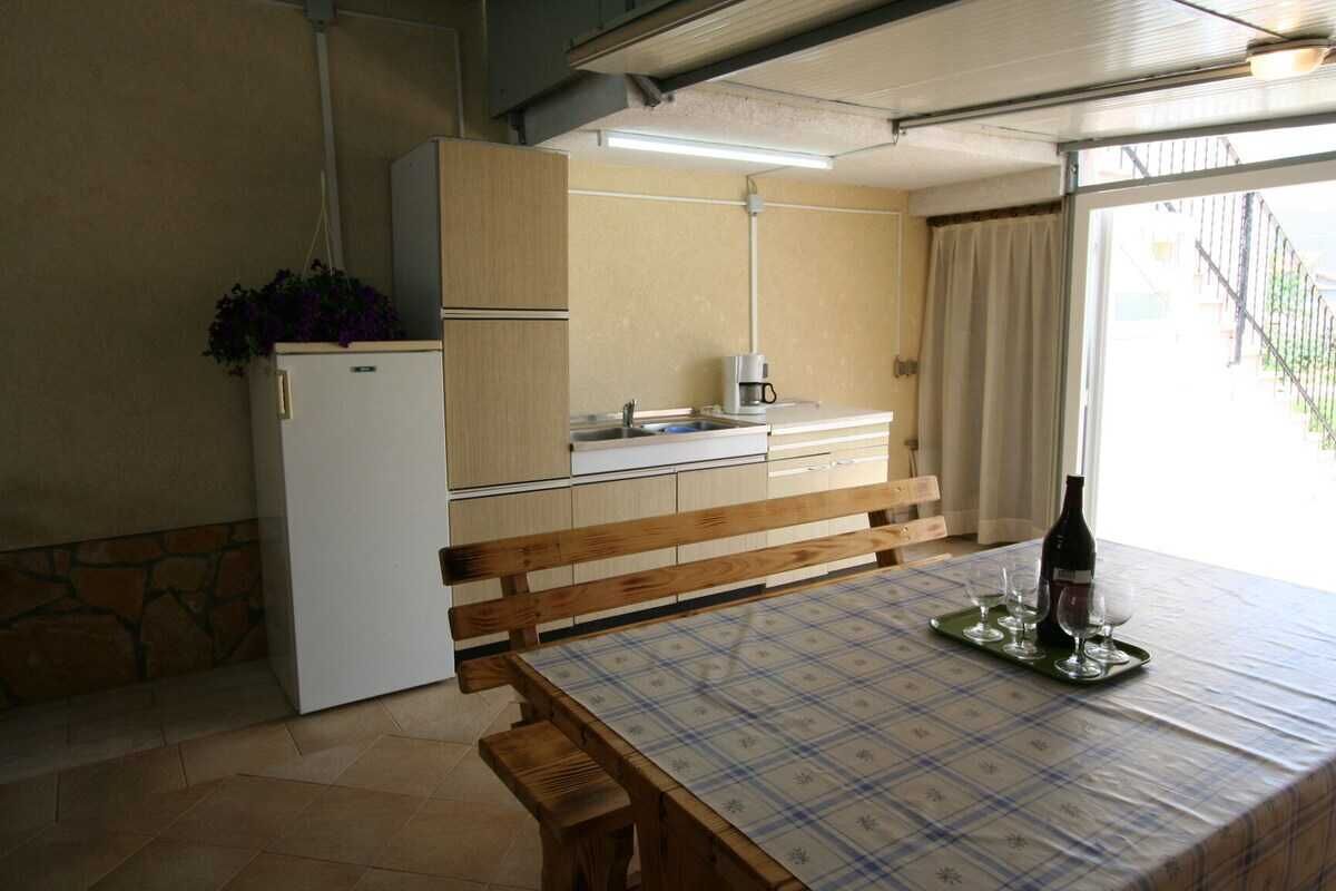 Une cuisine compacte comprenant un réfrigérateur, un banc, une table avec un set de table et une fenêtre avec des rideaux.