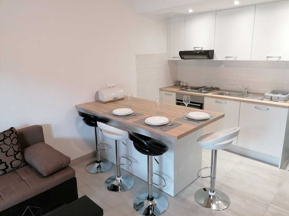 A modern kitchen with a central island, bar stools, a sofa, and a dining table.