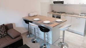 A modern kitchen with a central island, bar stools, a sofa, and a dining table. - Apartment Grskovic G. Setaliste A2 (Silo - island Krk)