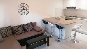 A modern living room with a sofa, a coffee table, and a kitchen area with a bar stool and a sink. - Apartment Grskovic G. Setaliste A2 (Silo - island Krk)