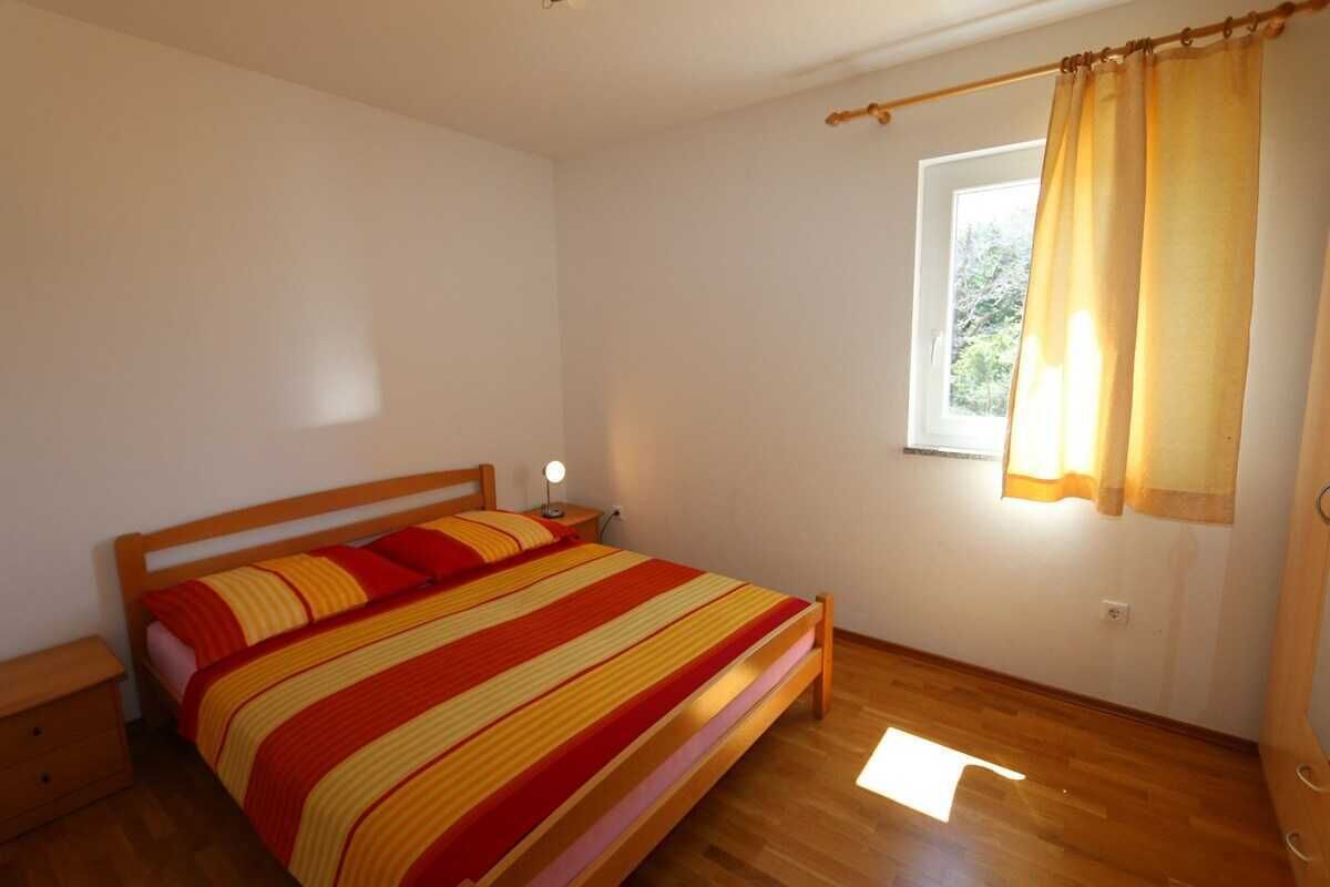 Ein Schlafzimmer mit einem hölzernen Bett, einem Nachttisch, einem Fenster mit Vorhängen und einem Holzboden.