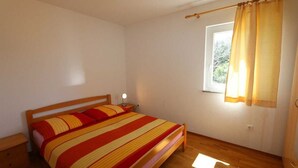 A bedroom with a wooden bed, a nightstand, a window with curtains, and a wooden floor. - Apartment Dudovic Damir A2 nr 2 (Silo - island Krk)