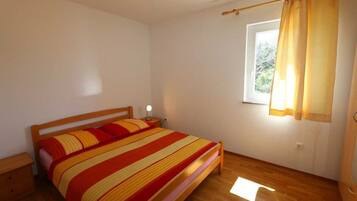 Ein Schlafzimmer mit einem hölzernen Bett, einem Nachttisch, einem Fenster mit Vorhängen und einem Holzboden.