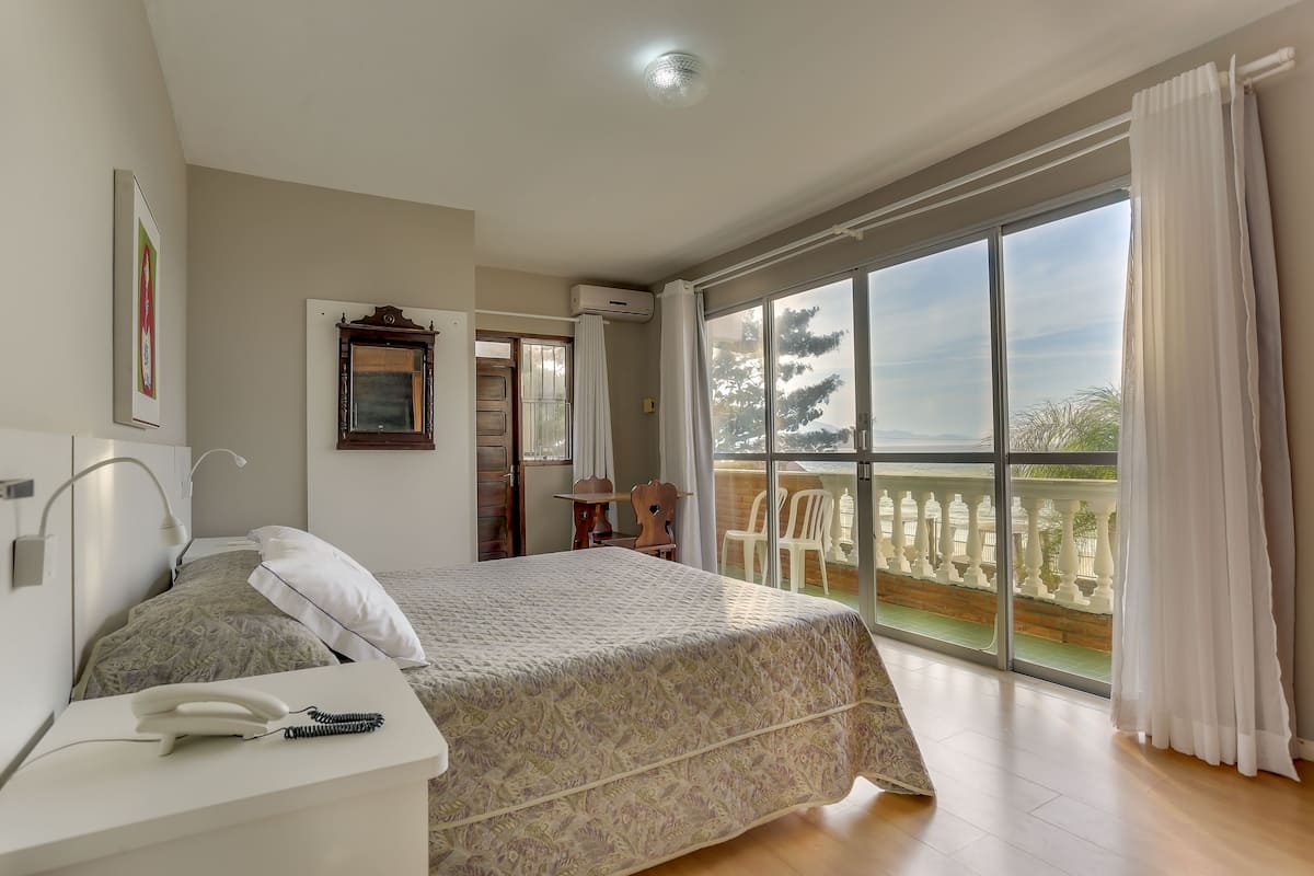 A bedroom with a bed, bedside table, and a view of a balcony.