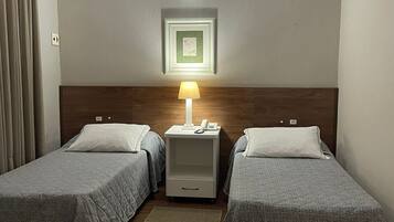 Habitación de hotel con dos camas individuales, una mesita de noche con lámpara, un cuadro enmarcado en la pared y un cabecero de madera.