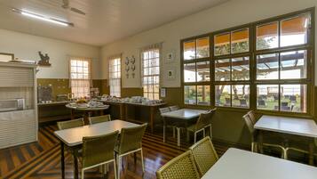 A dining area with tables and chairs, a kitchen area with appliances, and large windows with views of the outdoors.