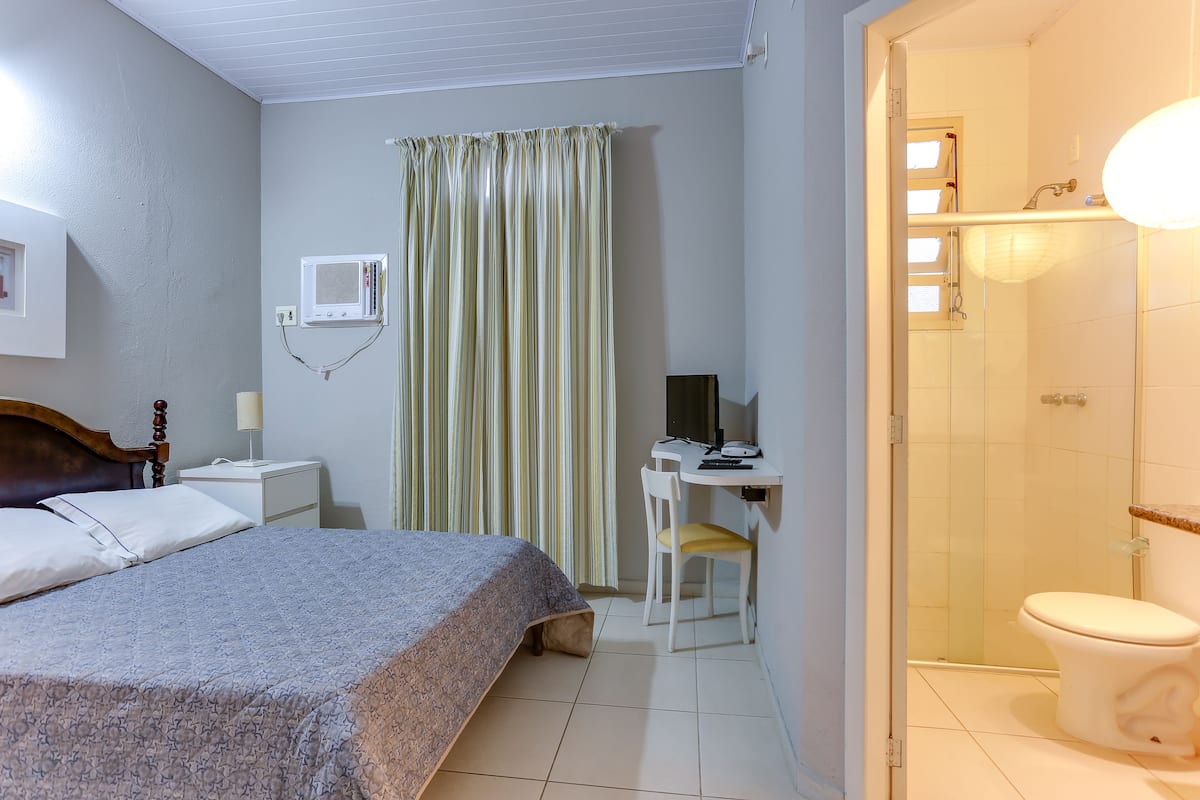 A hotel room with a bed, a desk with a chair, a shower, and a toilet.