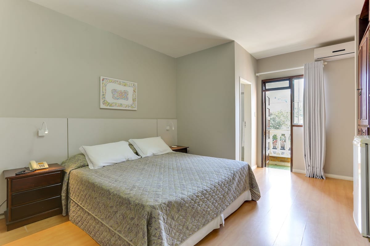 A bedroom with a bed, bedside tables, a nightstand, a wall-mounted telephone, and a window with curtains.