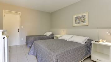 A room with two beds, a white bedside table with a lamp, a framed artwork on the wall, and a door.