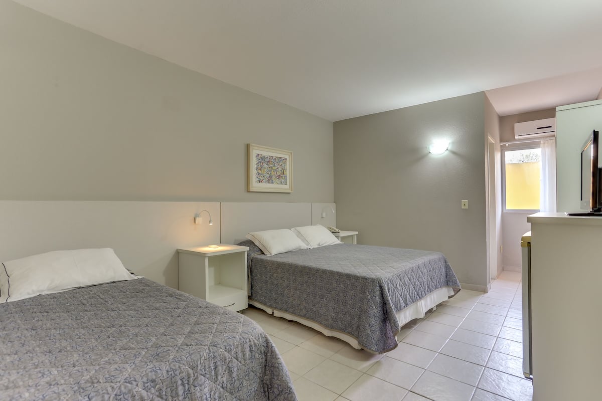 A bedroom with two beds, a nightstand, a wall-mounted light, and a door leading to another room.