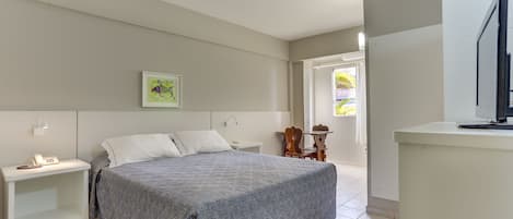 Un dormitorio con cama, mesitas de noche, escritorio, silla y televisor.
