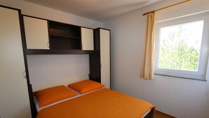 A bedroom with a bed, a window with curtains, and built-in storage cabinets. - Apartment Dudovic Darko nr 4 (Silo - island Krk)
