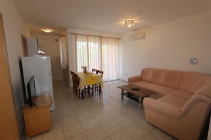 A living room with a sofa, a coffee table, a TV on a stand, a dining table with chairs, and a kitchen area with a refrigerator. - Apartment Dudovic Darko nr 4 (Silo - island Krk)