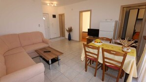 A living room with a sofa, a coffee table, a dining table with chairs, a TV, and a refrigerator. - Apartment Dudovic Darko nr 4 (Silo - island Krk)