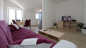 A living room with a sofa, a coffee table, a TV, and a dining area with chairs and a table. - Apartment Sucic Tea 4 (Soline - island Krk)